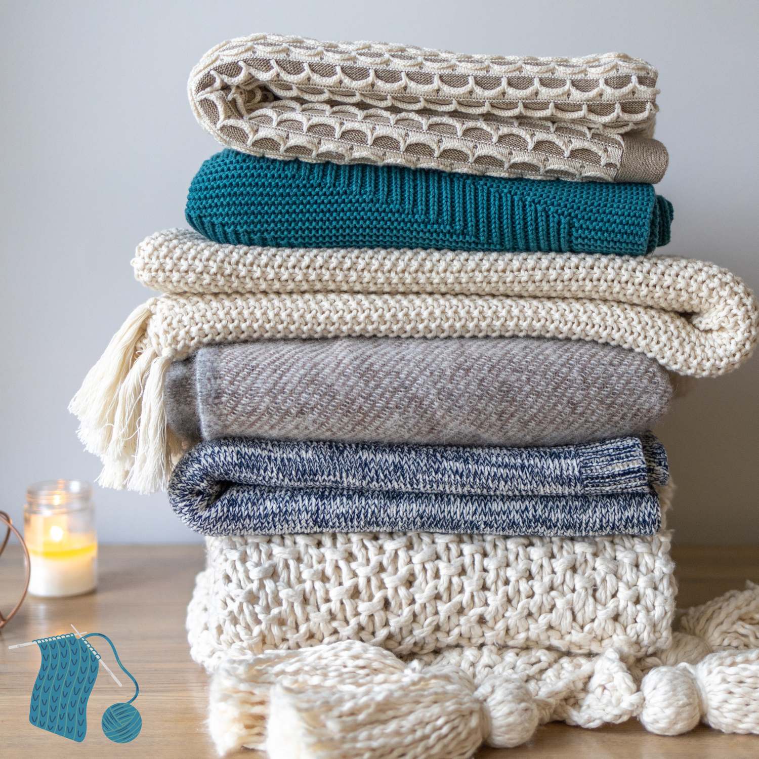 Pile fo white grey and teal knitting items with candle